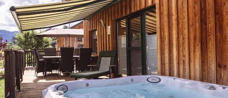 Una cabaña de madera con hidromasaje, mobiliario exterior y un porche cubierto.