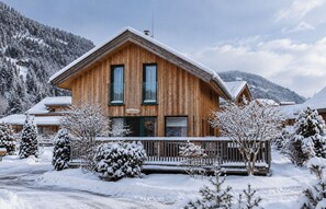 Eine Holzhütte mit Balkon, umgeben von schneebedeckten Bäumen und Bergen.
