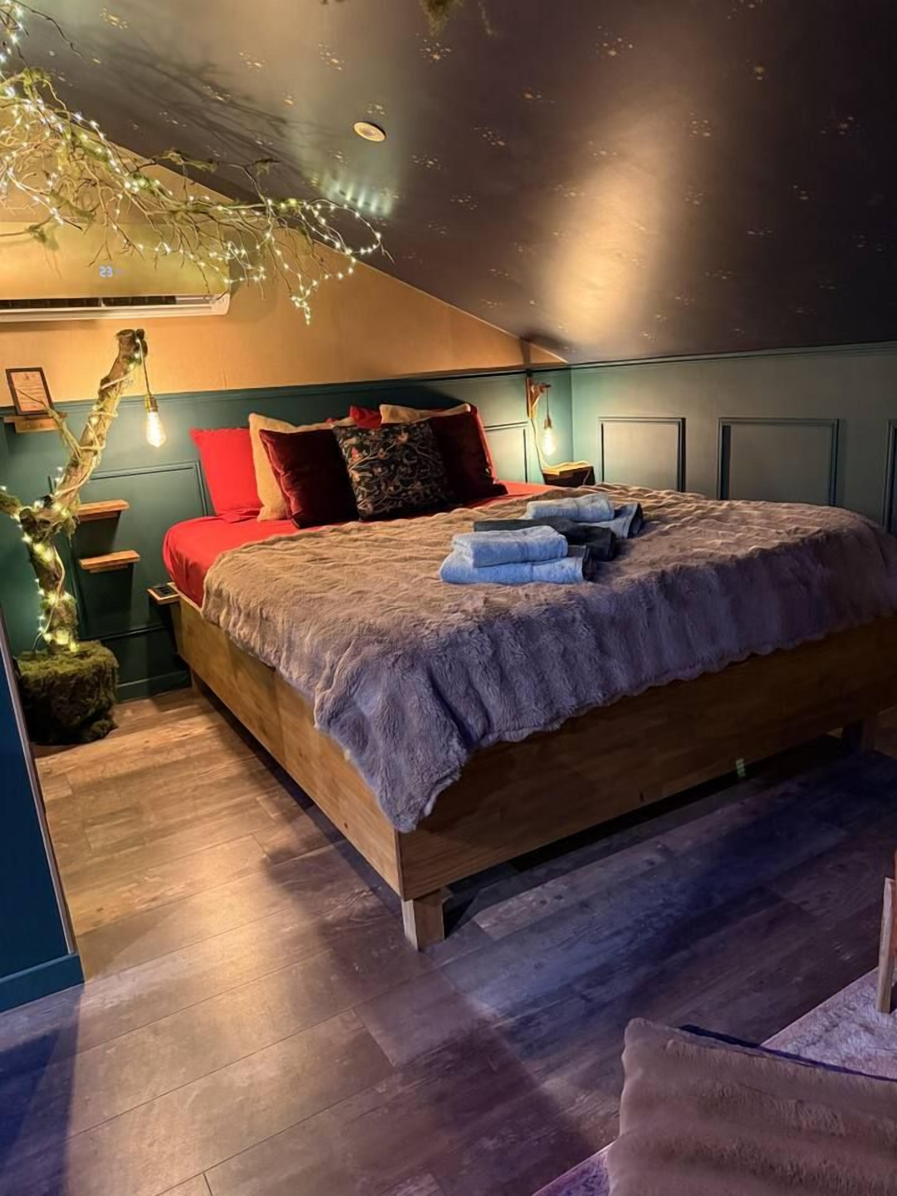 A bedroom with a wooden bed, red and patterned pillows, a small side table, and a wall-mounted air conditioner.