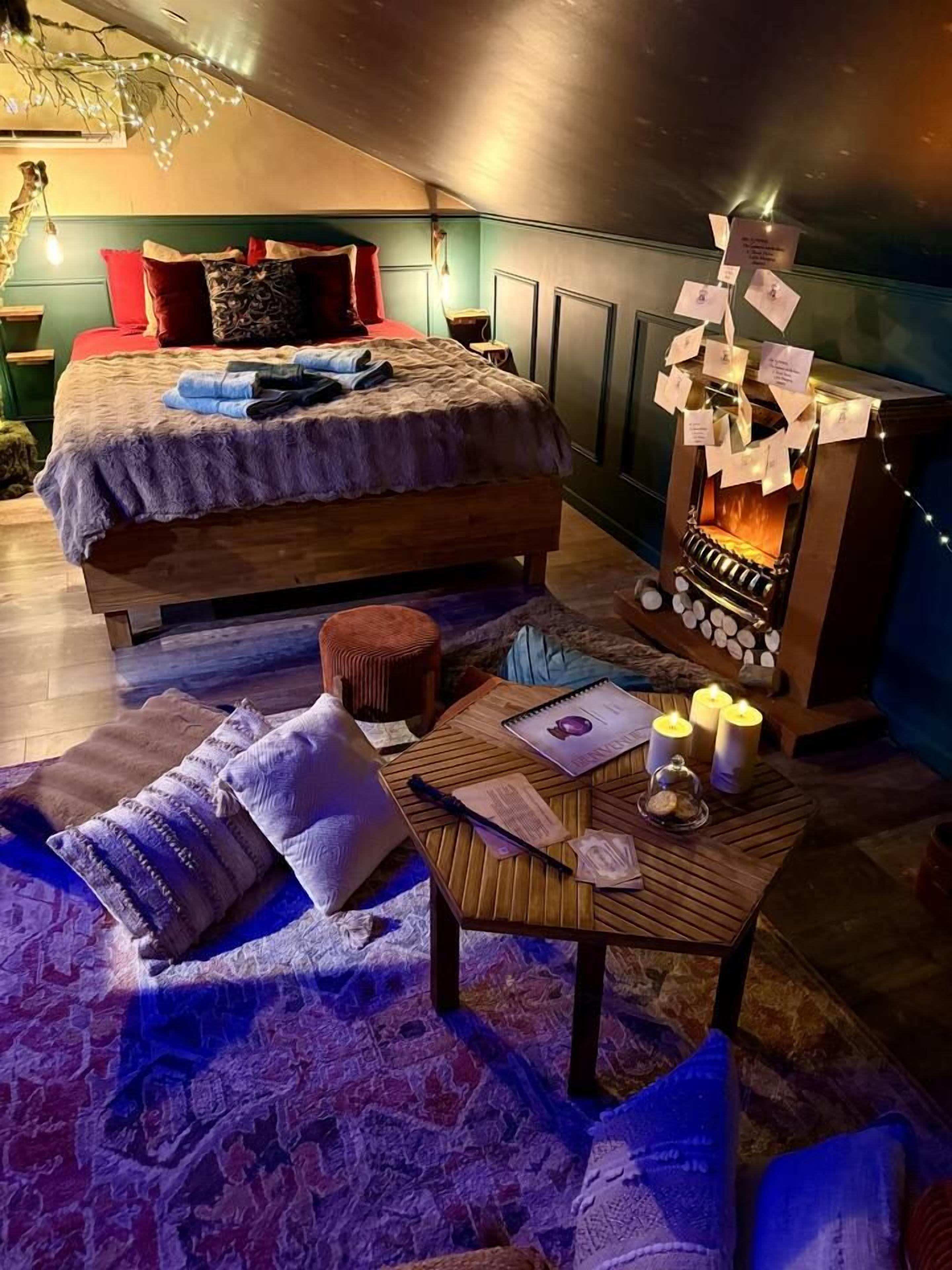 Um quarto aconchegante com cama, uma mesinha com velas e uma lareira.