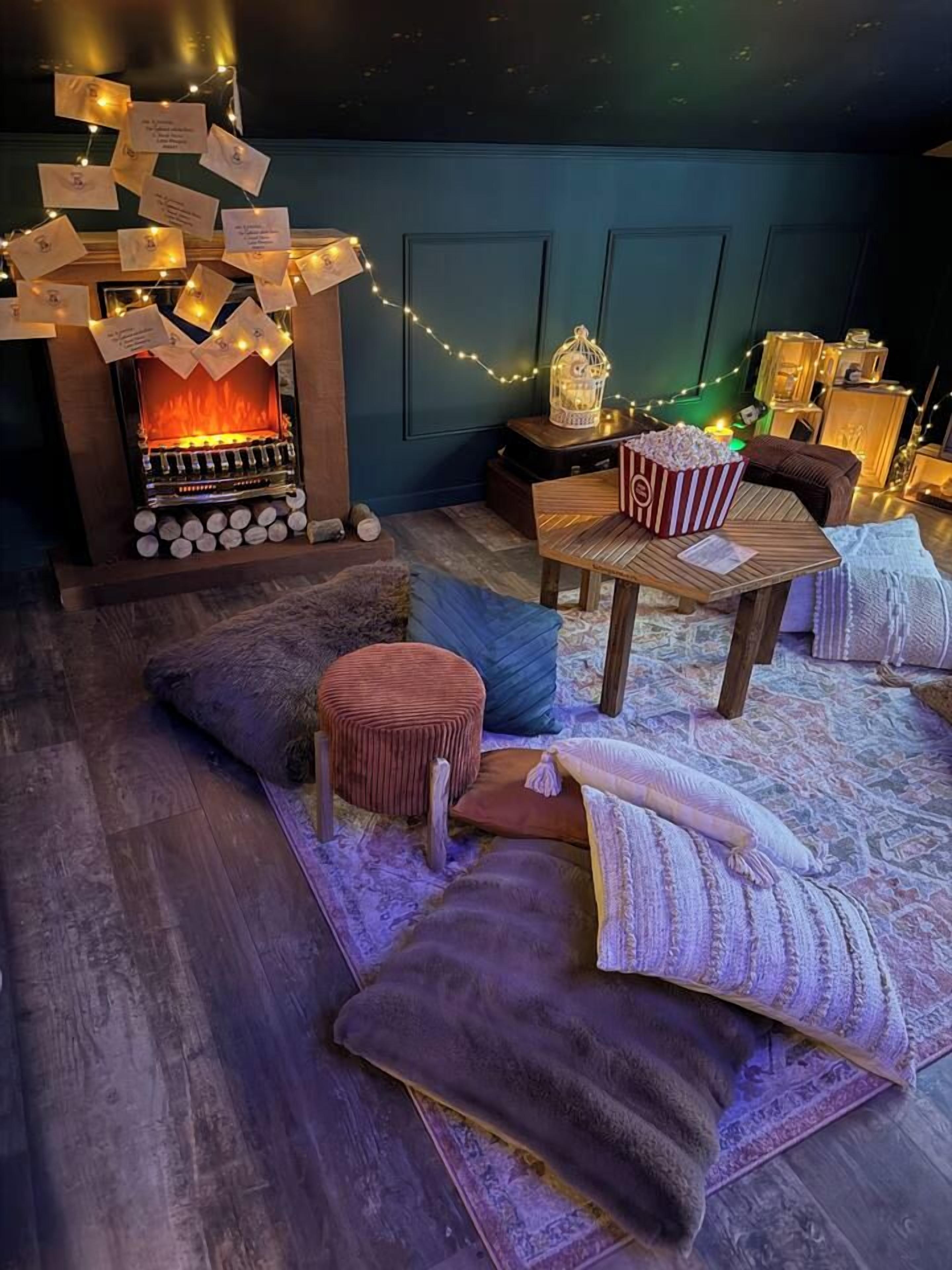 A cozy room with a fireplace, a comfortable seating area with cushions and a small ottoman, and a table with a popcorn bucket.