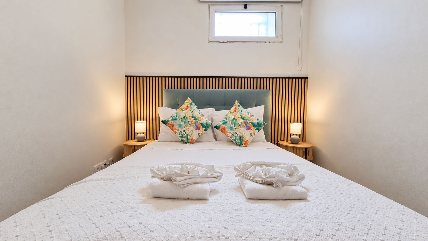 A hotel room with a bed, two nightstands, a window, and a headboard with vertical slats.