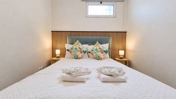 Habitación de hotel con una cama, dos mesitas de noche, un ventanal y un cabecero con listones verticales.