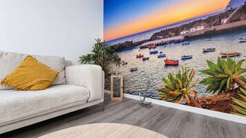 Una sala de estar con un sofá, una planta y vista a barcos en el agua.