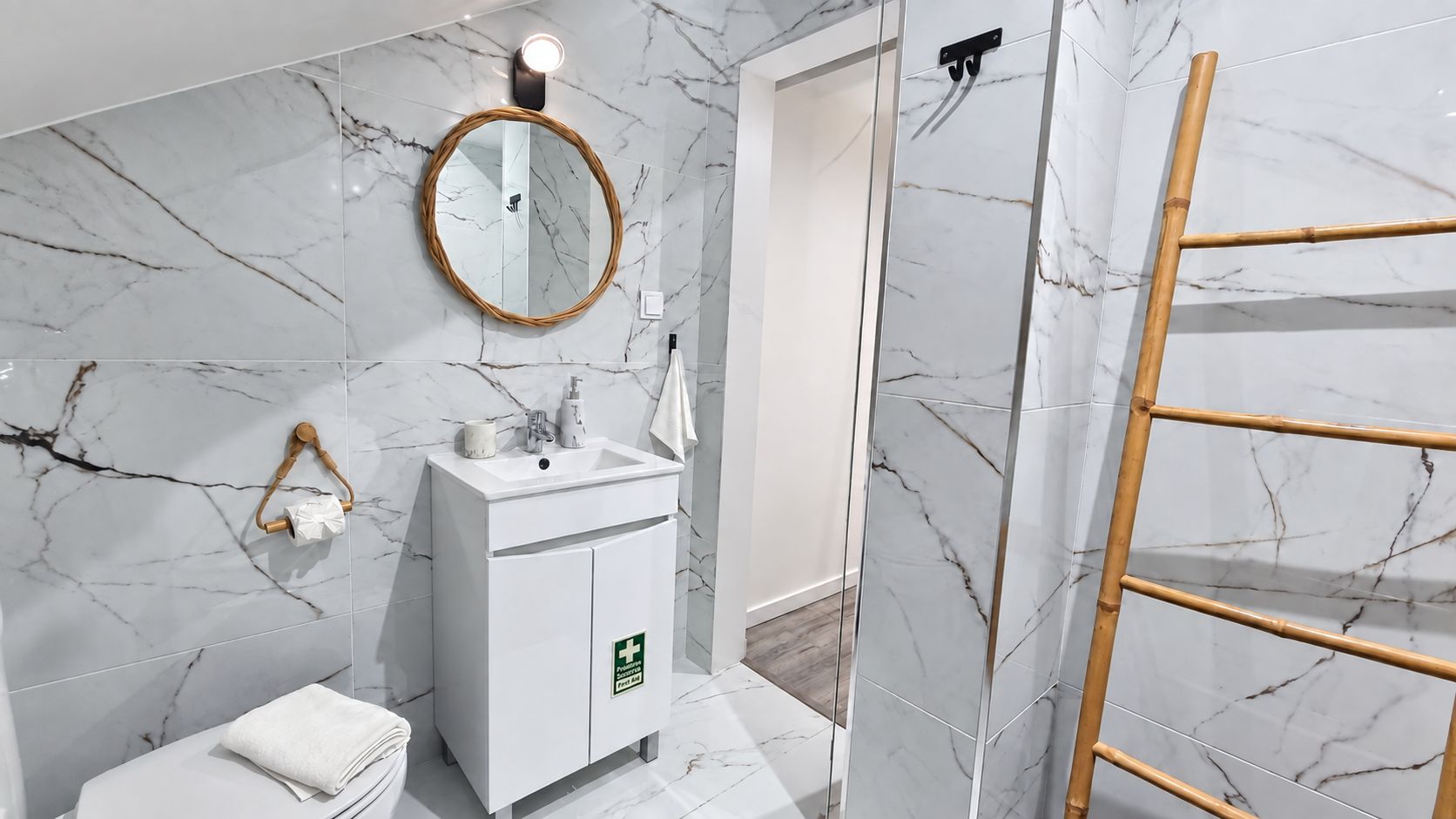 Une salle de bain avec un mur en marbre, un lavabo blanc, un miroir, un porte-serviettes et une échelle en bois.