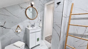 Une salle de bain avec un mur en marbre, un lavabo blanc, un miroir, un porte-serviettes et une échelle en bois.