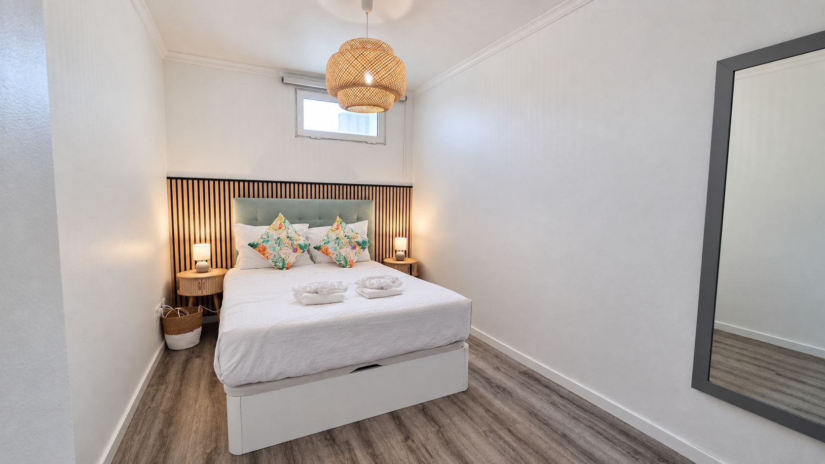 Une chambre à coucher moderne avec un lit, des lampes de chevet, un luminaire suspendu et un grand miroir.