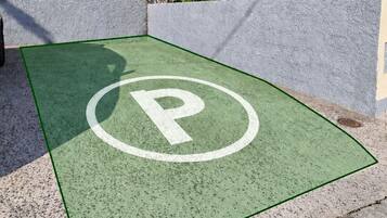 Un estacionamiento con superficie verde y un símbolo de 'P' blanco, rodeado de escalones de piedra y un edificio con balcones.