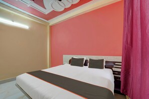 A hotel room with a bed, a headboard, and a window with curtains.