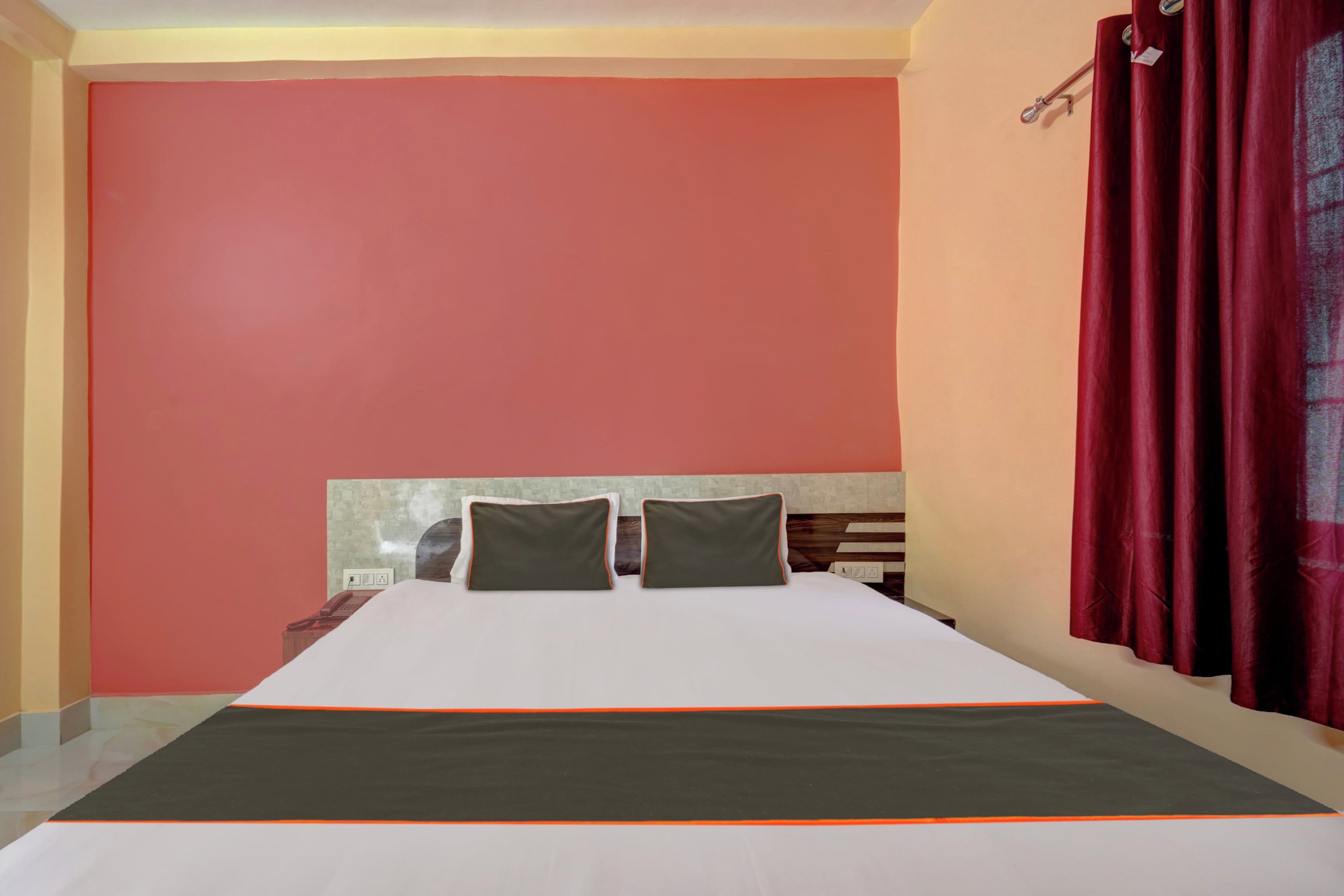Habitación de hotel con cama, dos almohadas, mesita de noche y cortina roja.