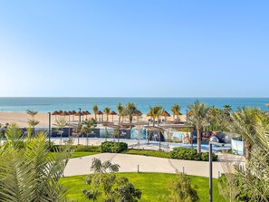 Een resort met een zwembad, palmbomen en uitzicht op het strand.