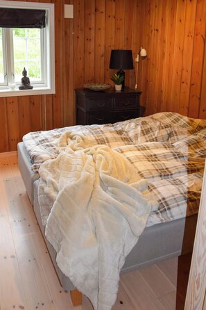A bedroom with a bed, wooden walls, a window with a view, a nightstand with a lamp, and a small Buddha statue. - Cabin 50m from cross-country trail on Tempelseter (Eggedal)