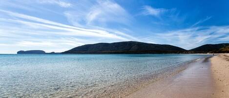 A beach with clear water, a sandy shore, and distant hills.
