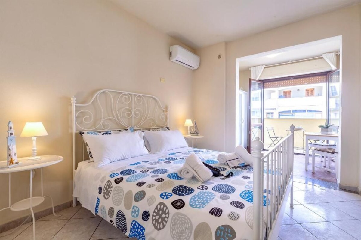Une chambre d’hôtel comprenant un lit, deux tables de chevet, un appareil de climatisation et un balcon avec vue sur l’immeuble.