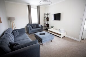 A modern living room with a grey sofa, a matching ottoman, a white side table, and a bookshelf. - 17 Larchfield House  (Darlington)