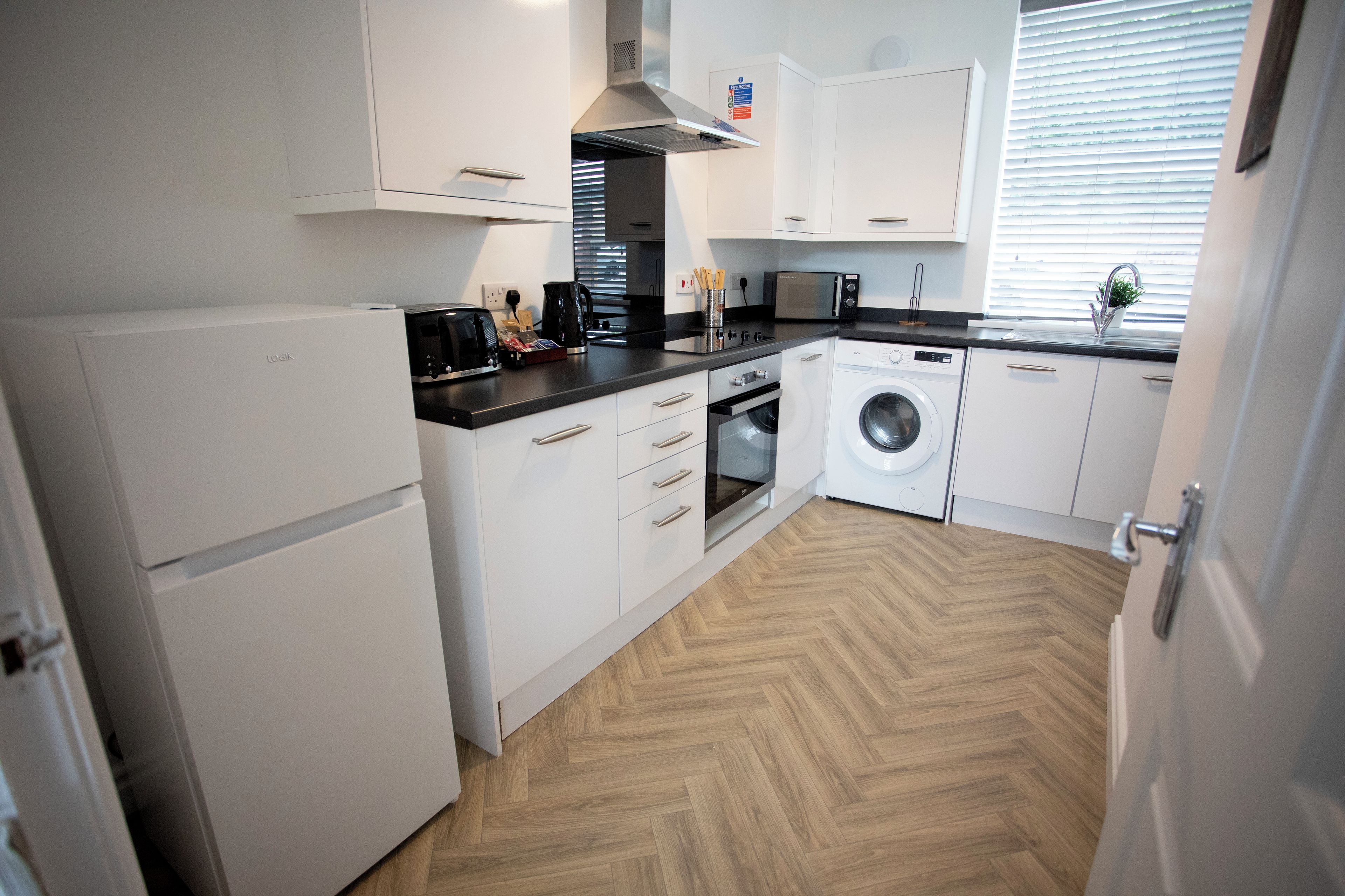 A compact kitchen with white cabinets, a built-in oven, a microwave, and a washing machine.
