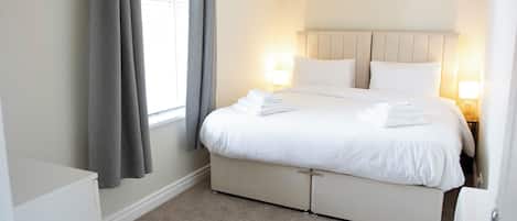 A hotel room with a bed, bedside lamps, a window with curtains, and a radiator.