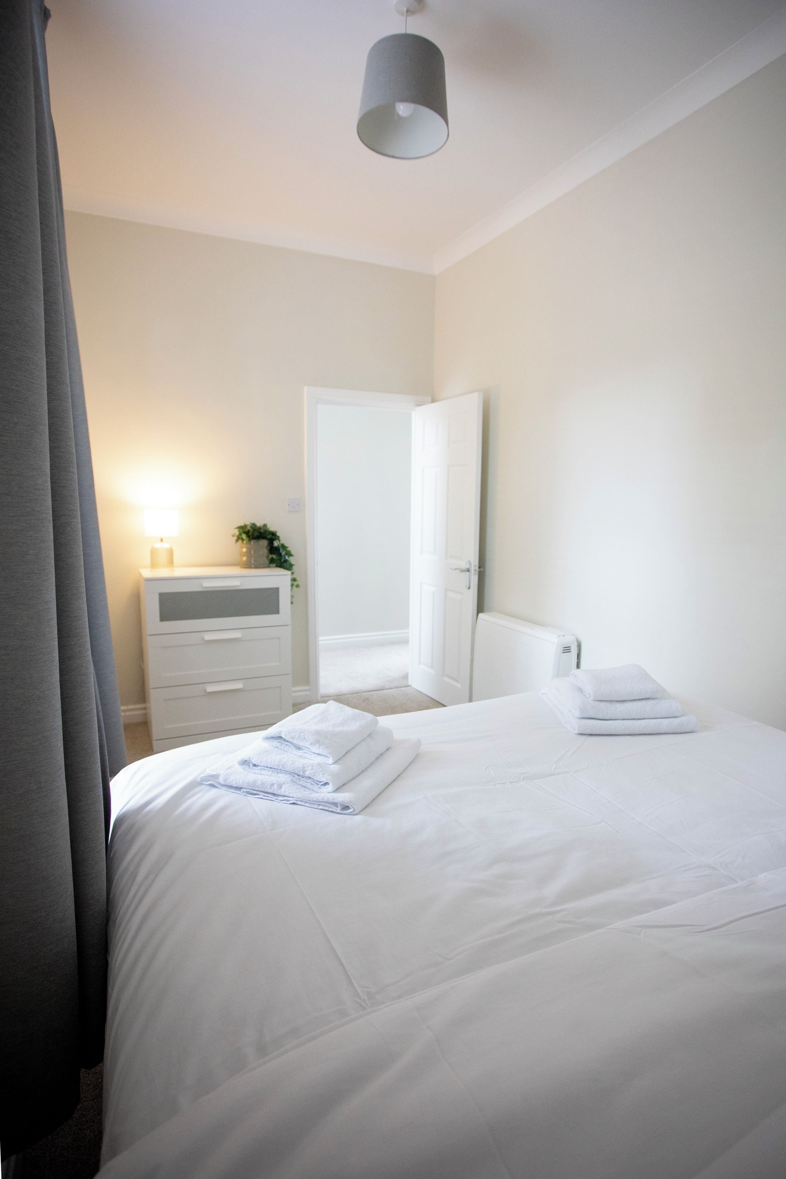 A hotel room with a bed, a bedside table with a lamp, a dresser, and a door.