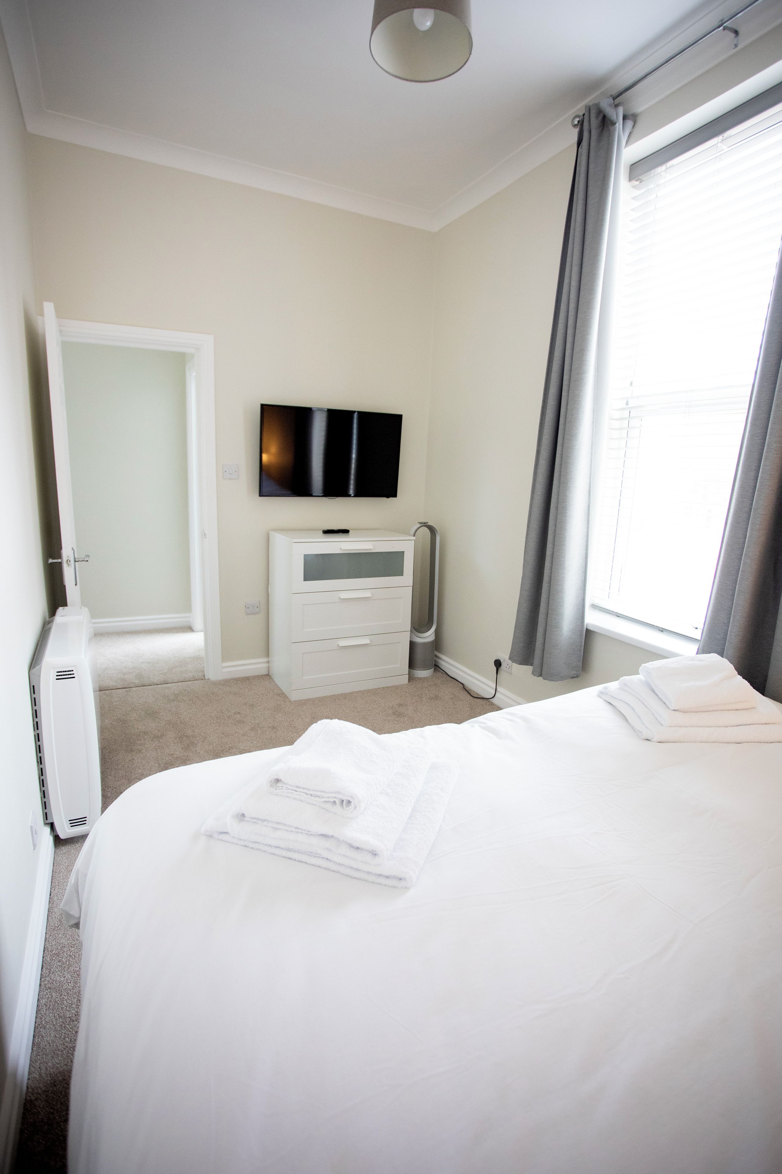 Una habitación de hotel con cama, televisión, cómoda y ventana con cortinas.