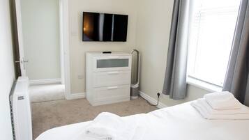 Una habitación de hotel con cama, televisión, cómoda y ventana con cortinas.