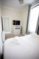 A hotel room with a bed, a television, a dresser, and a window with curtains.