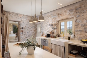 A kitchen with stone walls, a dining area with a table and chairs, and a window with a view.