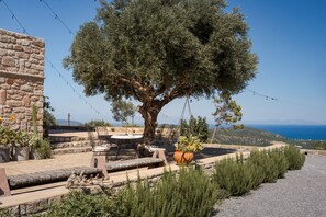 Un edificio de piedra con terraza al aire libre, un árbol grande y vistas al mar.