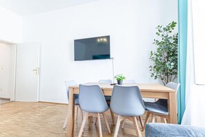 Ein Konferenzraum mit Holztisch, grauen Stühlen, einem an der Wand befestigten Flachbildfernseher und einer Zimmerpflanze.