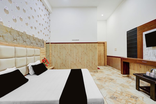 A hotel room with a large bed, a wooden headboard, a wall with a geometric pattern, a wooden partition, a wooden desk with a mirror, and a marble floor.