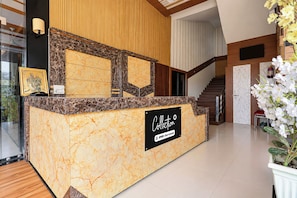 A reception desk with a marble finish, a sign indicating it is serviced by OYO, and a staircase in the background.