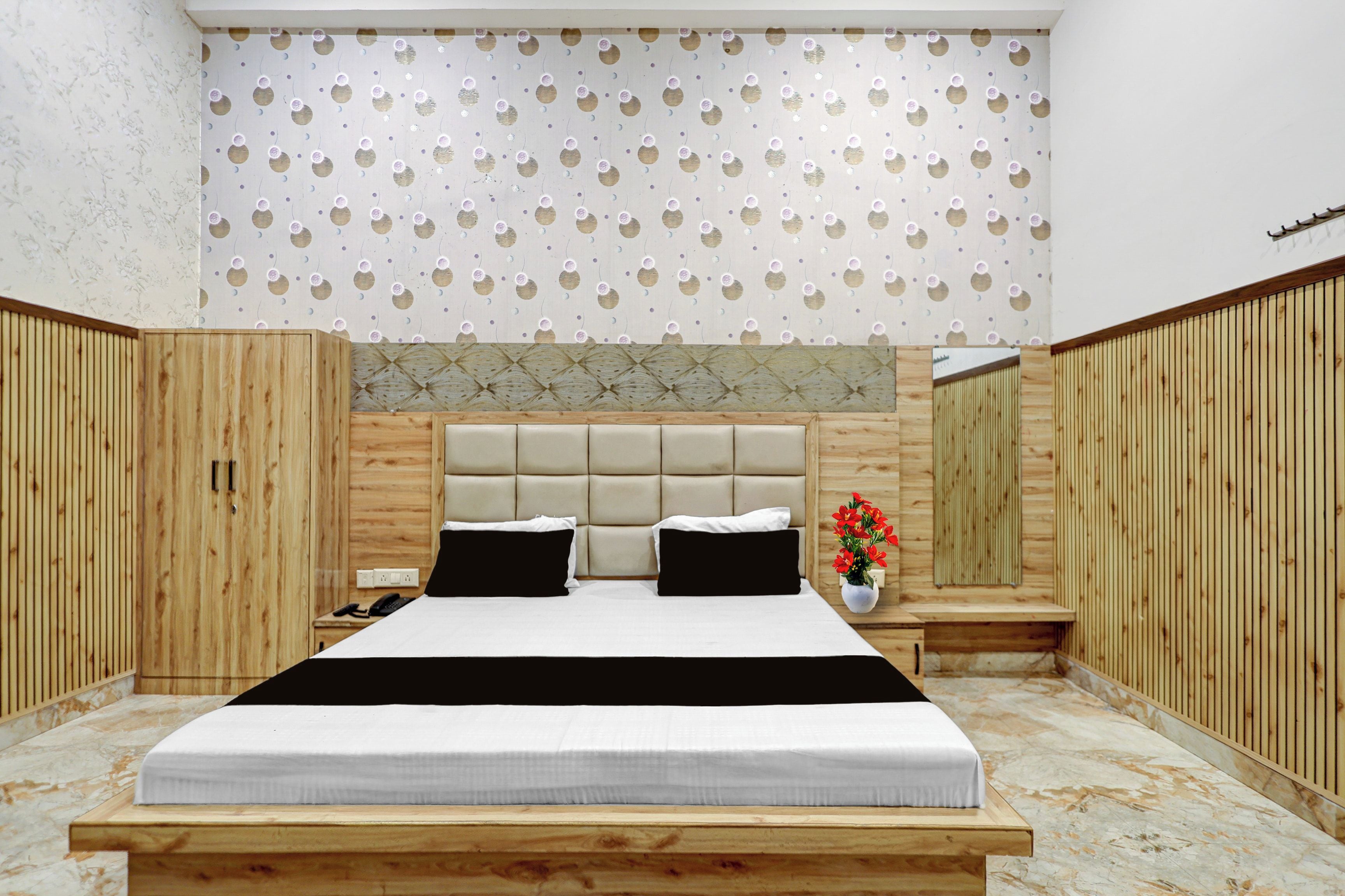 Une chambre avec un grand lit, des lambris en bois sur les murs, un plafond décoré et une petite table de chevet sur laquelle est posé un vase rempli de fleurs.