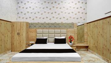 Une chambre avec un grand lit, des lambris en bois sur les murs, un plafond décoré et une petite table de chevet sur laquelle est posé un vase rempli de fleurs.