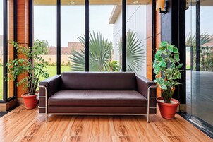 A brown leather sofa in a modern room with large windows, wooden flooring, and potted plants.