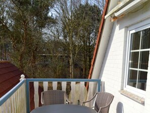 A balcony with wicker chairs, a white building with a window, and trees in the background. - Holiday Apartment With 1 Bedroom (Wyk auf Foehr)
