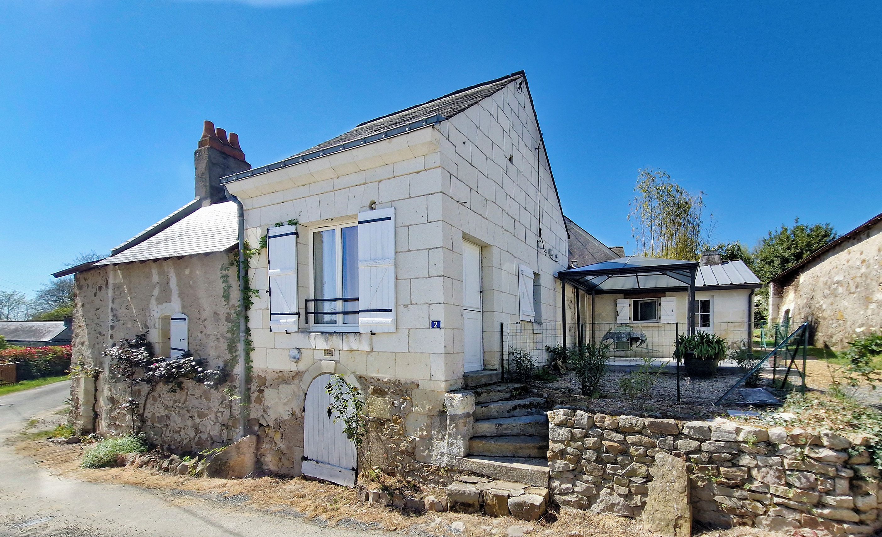 Un bâtiment en pierre avec un toit en tuiles, un petit porche et un mur de pierre à l’avant.