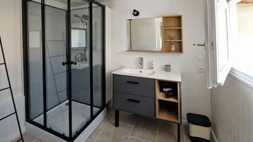 A bathroom with a glass-enclosed shower, a white sink, a mirror, and a small shelf with toiletries.