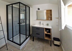 Une salle de bain avec une douche à parois de verre, un lavabo blanc, un miroir et une petite étagère contenant des articles de toilette.