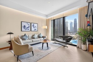 A modern living room with a sofa, armchair, coffee table, and a large window with a city view. - 3BR Address Opera High Floor Burj View (Dubai)
