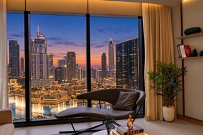 A modern living room with a large window overlooking a cityscape at dusk. - 3BR Address Opera High Floor Burj View (Dubai)