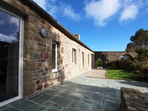 A stone building with a paved pathway leading to an arched stone bridge. - Norman Longhouse with Garden and Pets Allowed (La Hague)