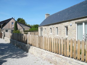 A stone building with a wooden fence, a gravel driveway, and a clear sky. - Norman Longhouse with Garden and Pets Allowed (La Hague)