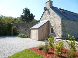Un bâtiment en pierre avec un toit en pente, un abri en bois et une allée gravillonnée.