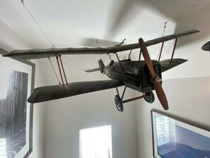 Un avió biplà vintage penjat del sostre d'una habitació amb grans finestres i quadres emmarcats.