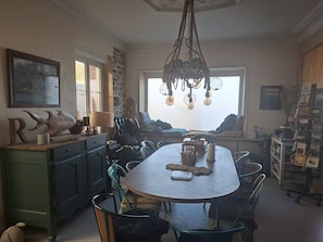 En spiseplads med et stort, ovalt bord, grønne stole, en hængende lampe og en stenvæg.