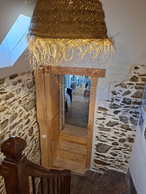 Eine Holztreppe führt zu einem Dachbodenbereich mit einem Reetdach und Lichterketten.