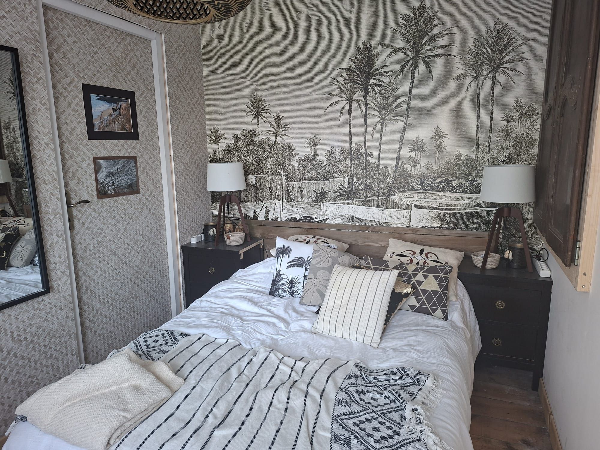A bedroom with a bed, pillows, a nightstand, a lamp, a mirror, and a wall tapestry.