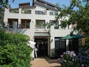 A two-story building with a ground-level entrance, a balcony with railings, and a covered outdoor seating area. - Above the Rooftops of Wyk/ Near the Beach (Wyk auf Foehr)