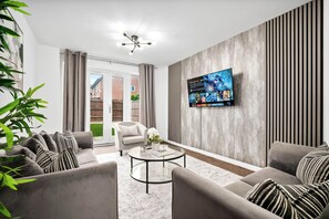 Ein modernes Wohnzimmer mit einer Sofagarnitur, einem Couchtisch und einem an der Wand montierten Flachbildfernseher.