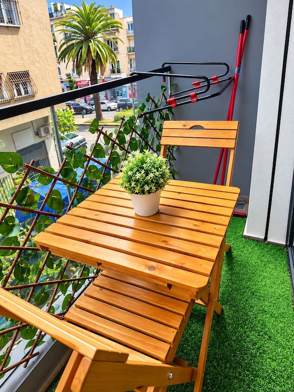 En balkon med et træbord og stole, en potteplante og udsigt til gaden.
