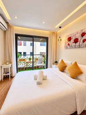 Ein Hotelzimmer mit einem großen Bett, einem Gemälde, einem kleinen Tisch mit einer Uhr und Blick auf den Balkon.